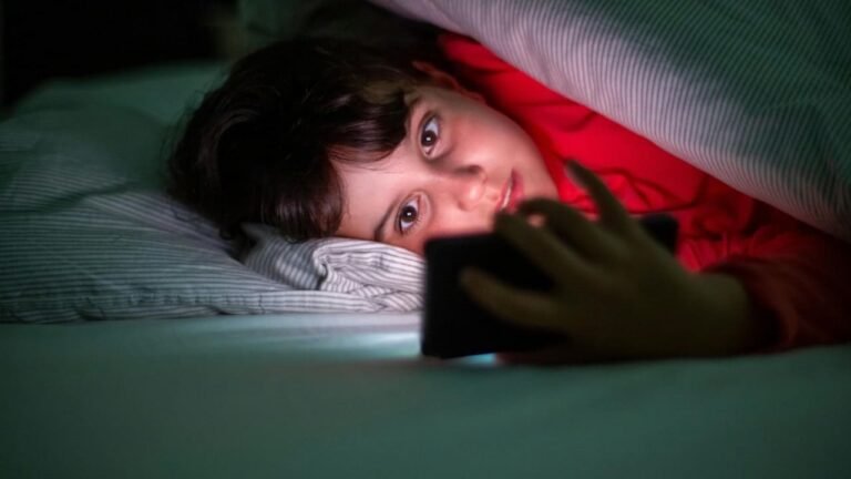 A child using a smartphone under the covers at night, showing the negative effects of social media use.