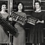 Four women holding components of the ENIAC computer, the first electronic digital computer, standing in front of its panels.