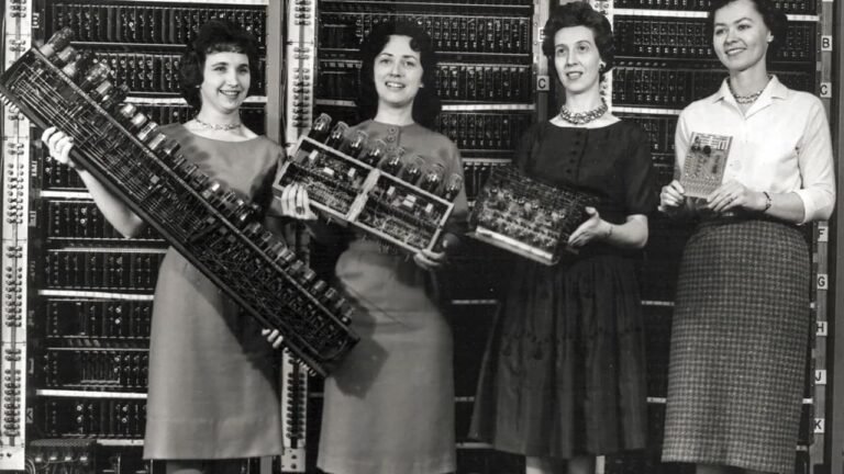 Four women holding components of the ENIAC computer, the first electronic digital computer, standing in front of its panels.